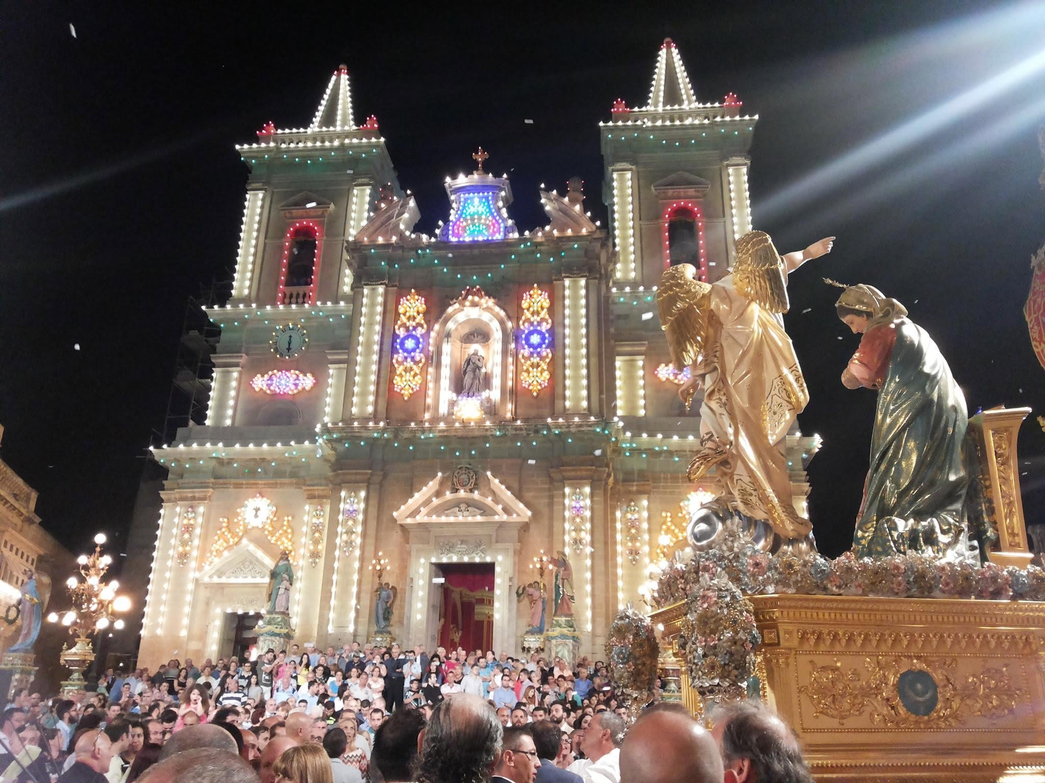 Annunciation statues and a crowd outside the illuminated church