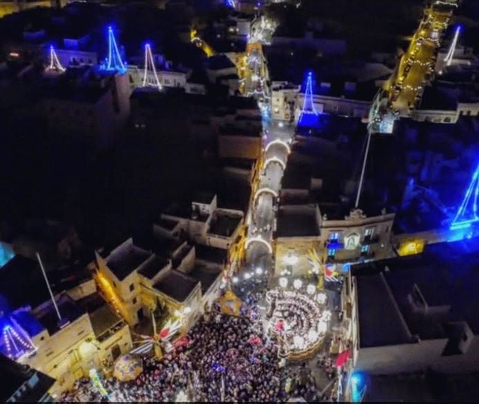 A crowd and illuminated village streets viewed from above