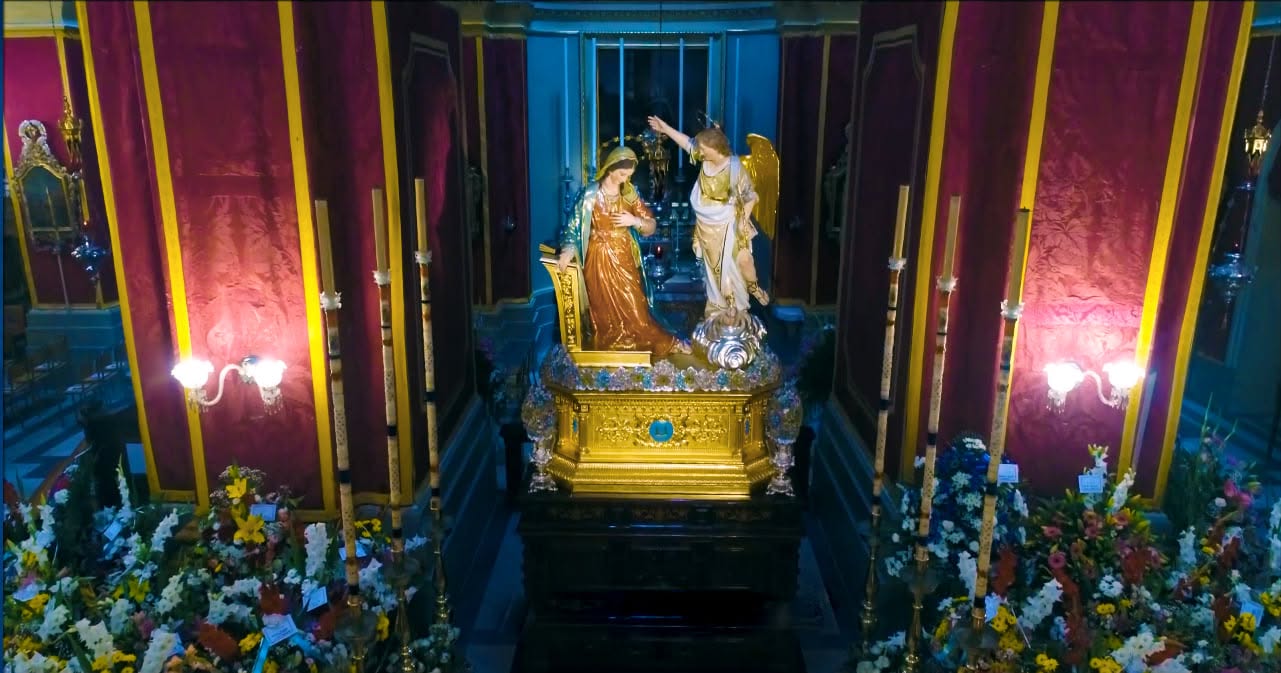 Annunciation statues displayed with flowers and candles