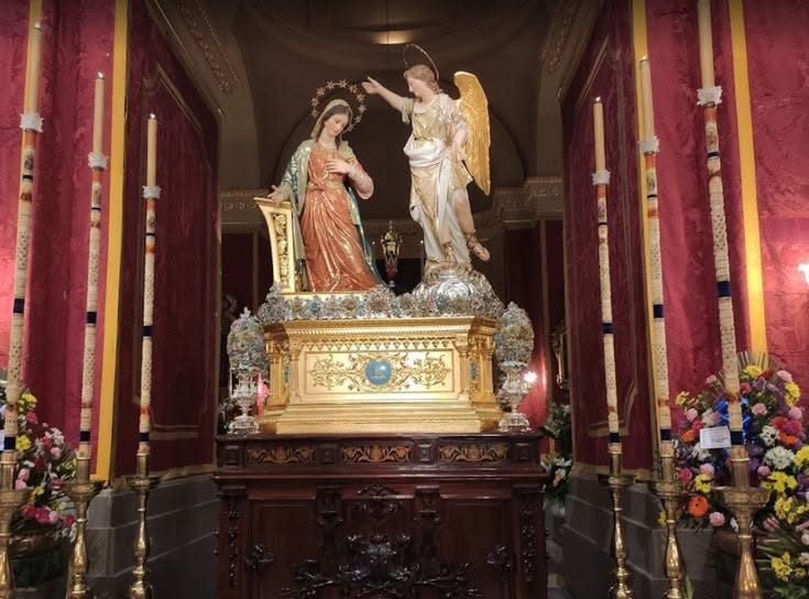 Annunciation statues displayed inside the church, surrounded by candles and flowers